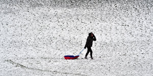 Eine Frau mit einem Schlitten geht über eine schneebedeckte Wiese.