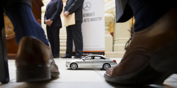 Ein Mercedes Spielzeugauto steht zwischen zwei Lederschuhen Ein Mercedes Spielzeugauto steht zwischen zwei Lederschuhen
