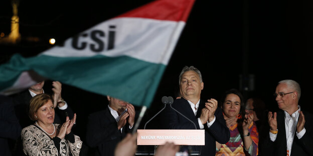 Orban klatscht in die Hände, neben ihm eine Flagge Orban klatscht in die Hände, neben ihm eine Flagge