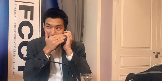 Juanggroongruangkit sitzt an einem Tisch und telefoniert per Handy; seinen Mund verdeckt er mit seiner Hand Juanggroongruangkit sitzt an einem Tisch und telefoniert per Handy; seinen Mund verdeckt er mit seiner Hand
