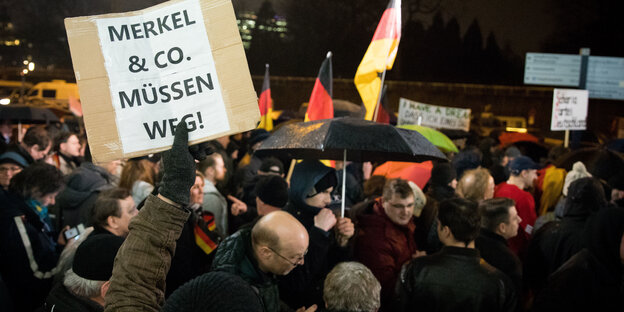 Demonstranten mit Deutschlandfahnen und "Merkel muss weg"-Schild. Demonstranten mit Deutschlandfahnen und "Merkel muss weg"-Schild.