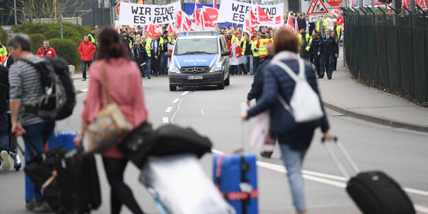 Reisende mit Koffern, im Hinergrund Verdi-Demo