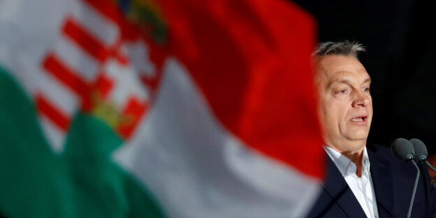 Viktor Orbán, neben ihm eine Ungarnflagge mit Wappen Viktor Orbán, neben ihm eine Ungarnflagge mit Wappen