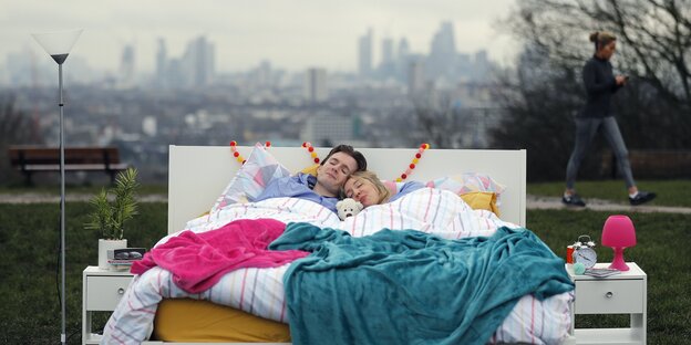 Zwei Menschen liegen aneinandergekuschelt in einem Bett, das unter freiem Himmel steht Zwei Menschen liegen aneinandergekuschelt in einem Bett, das unter freiem Himmel steht