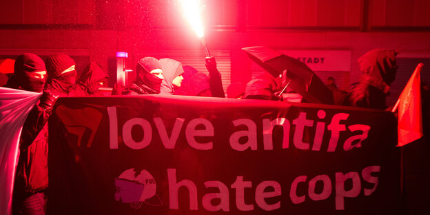 Schwarz gekleidete und vermummte Demonstranten tragen ein Transparent mit der Aufschrift "love antifa, hate cops". Schwarz gekleidete und vermummte Demonstranten tragen ein Transparent mit der Aufschrift "love antifa, hate cops".
