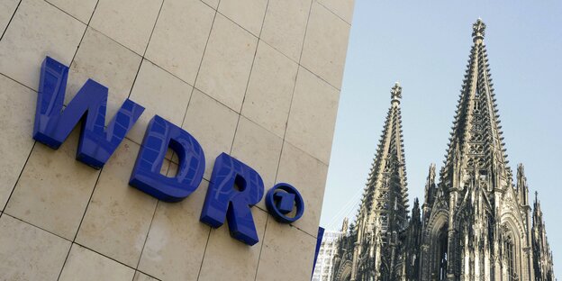 Das Logo des WDR an einer Hausfassade, daneben der Kölner Dom