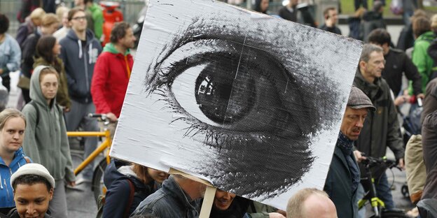 Demonstranten und ein Plakat mit einem Auge Demonstranten und ein Plakat mit einem Auge