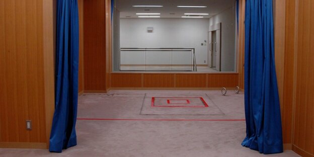 Ein Raum, blaue Vorhänge an den Seiten, auf dem grauen Teppich ist ein rotes Quadrat markiert Ein Raum, blaue Vorhänge an den Seiten, auf dem grauen Teppich ist ein rotes Quadrat markiert