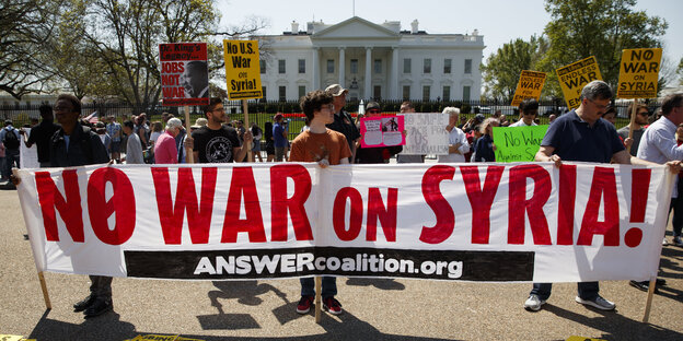 Im Hintergrund das Weiße Haus, im Vordergrund Menschen, die ein Plakat hochhalten, auf dem steht „No War on Syria“ Im Hintergrund das Weiße Haus, im Vordergrund Menschen, die ein Plakat hochhalten, auf dem steht „No War on Syria“