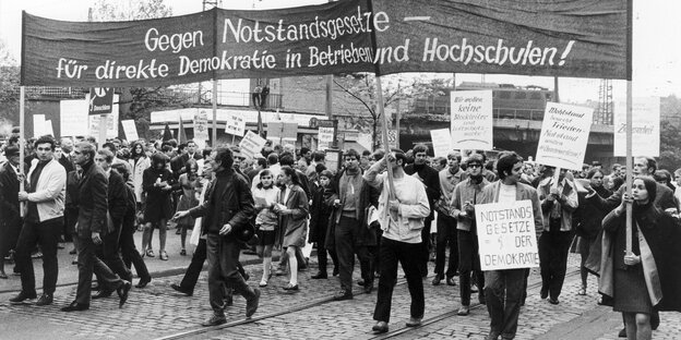 Schwarzweiß-Foto: Viele Menschen unter einem großen, in die Höhe gehaltenen Banner Schwarzweiß-Foto: Viele Menschen unter einem großen, in die Höhe gehaltenen Banner