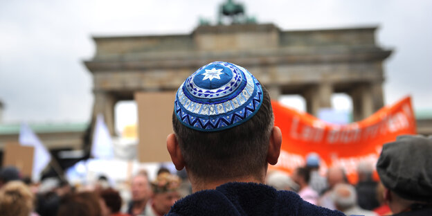 Ein Mann von hinten steht vor dem Brandenburger Tor in Berlin und trägt eine Kippa Ein Mann von hinten steht vor dem Brandenburger Tor in Berlin und trägt eine Kippa
