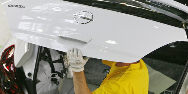 Ein Arbeiter trägt ein Teil eines Opel Corsa auf dem Kopf Ein Arbeiter trägt ein Teil eines Opel Corsa auf dem Kopf