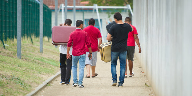 Flüchtlinge laufen mit Koffern bepackt auf einem Weg einer Erstaufnahmeeinrichtung