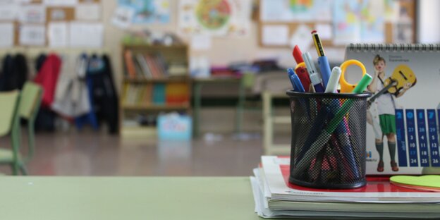 Ein Behälter mit Stiften und Schere steht auf einem Tisch in einem Klassenzimmer. Ein Behälter mit Stiften und Schere steht auf einem Tisch in einem Klassenzimmer.