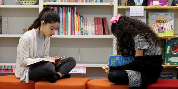 Zwei Mädchen sitzen vor einem Bücherregal und lesen. Zwei Mädchen sitzen vor einem Bücherregal und lesen.
