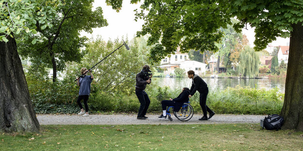 Ein Mann filmt einen Menschen in einem Rollstuhl im Park Ein Mann filmt einen Menschen in einem Rollstuhl im Park