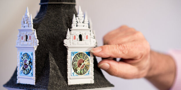 Ein Finger an einer Miniaturuhr Ein Finger an einer Miniaturuhr