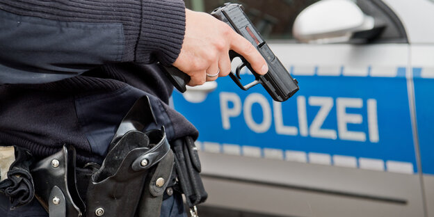Ein Polizist mit gezückter Waffe vor einem Polizeiauto Ein Polizist mit gezückter Waffe vor einem Polizeiauto