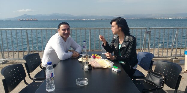 Ein Mann und eine Frau bei einem Snack an einem Tisch am Meer Ein Mann und eine Frau bei einem Snack an einem Tisch am Meer