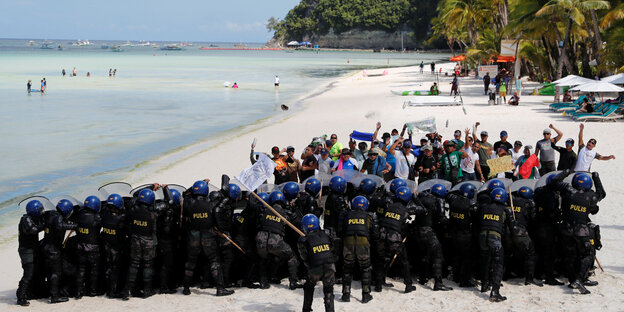 Uniformierte und Touristen stehen sich an einem Sandstrand mit Palmen gegenüber Uniformierte und Touristen stehen sich an einem Sandstrand mit Palmen gegenüber