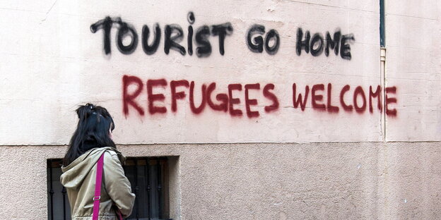 Eine Frau läuft an einer Wand vorbei, an die jemand "Tourists go home" und "Refugees Welcome" gesprüht hat Eine Frau läuft an einer Wand vorbei, an die jemand "Tourists go home" und "Refugees Welcome" gesprüht hat