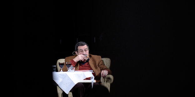 Günter Grass sitzt auf einer Bühne hinter einem Tisch mit zwei Gläsern Rotwein.