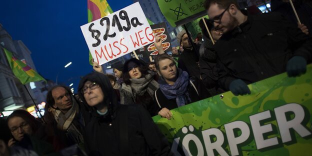 Viele Menschen stehen zusammen, manche halten Plakate, auf denen steht: Paragraf 219a muss weg! Viele Menschen stehen zusammen, manche halten Plakate, auf denen steht: Paragraf 219a muss weg!