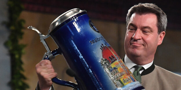 Ein Mann hält einen riesigen Bierkrug in der Hand und sieht ihn sich genau an Ein Mann hält einen riesigen Bierkrug in der Hand und sieht ihn sich genau an