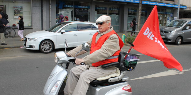 Ein Mann fährt mit dem Elektroroller und einer Flagge der Linkspartei Ein Mann fährt mit dem Elektroroller und einer Flagge der Linkspartei