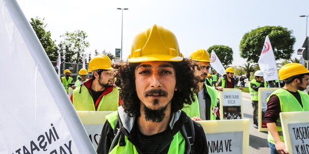 Mann mit Bauhelm, hinter ihm Demonstrierende Mann mit Bauhelm, hinter ihm Demonstrierende