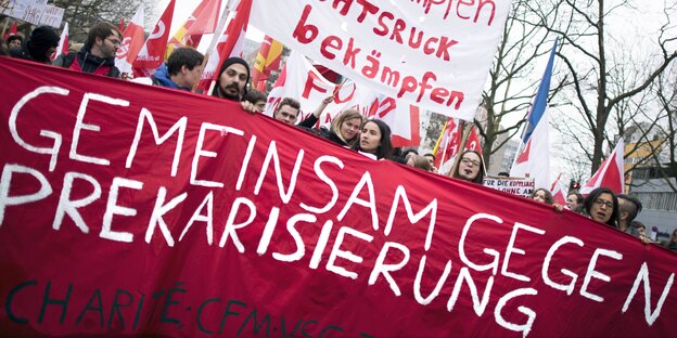 Menschen auf einer Kundgebung. Auf einem Transparent steht "Gemeinsam gegen Prekarisierung Menschen auf einer Kundgebung. Auf einem Transparent steht "Gemeinsam gegen Prekarisierung
