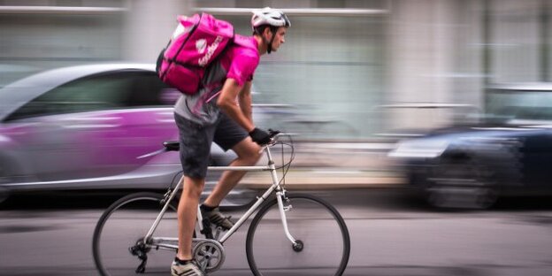 Ein Foodora-Kurier mit pinkem Rucksack fährt Fahrrad Ein Foodora-Kurier mit pinkem Rucksack fährt Fahrrad