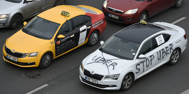 Ein Auto, das mit dem Schriftzug „stop uber" versehen ist, steht auf der Fahrbahn neben einem Taxi Ein Auto, das mit dem Schriftzug „stop uber" versehen ist, steht auf der Fahrbahn neben einem Taxi