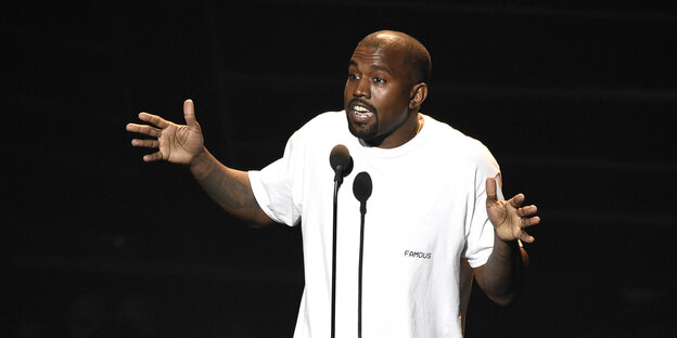Kanye West in weißem Hemd spricht ins Mikrophon und gestikuliert dabei Kanye West in weißem Hemd spricht ins Mikrophon und gestikuliert dabei