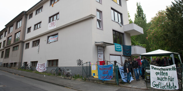 Vor einem Haus hängen Plakate und Menschen stehen vor dem Eingang. Vor einem Haus hängen Plakate und Menschen stehen vor dem Eingang.
