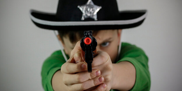 Ein Junge im Sherrifshut zielt mit einer Spielzeugpistole in die Kamera Ein Junge im Sherrifshut zielt mit einer Spielzeugpistole in die Kamera