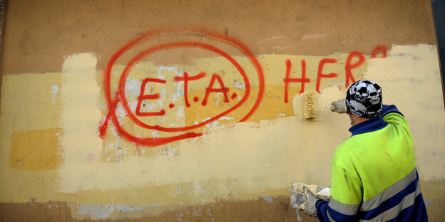Ein Maler überpinselt eine rote Schrift auf einer gelben Hauswand. "ETA" taucht darin auf; den Rest kann man nicht lesen Ein Maler überpinselt eine rote Schrift auf einer gelben Hauswand. "ETA" taucht darin auf; den Rest kann man nicht lesen