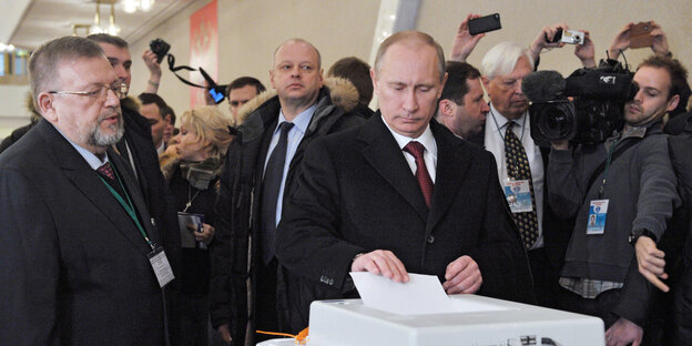 Putin steht an einer Wahlurne und gibt seinen Stimmzettel ab Putin steht an einer Wahlurne und gibt seinen Stimmzettel ab