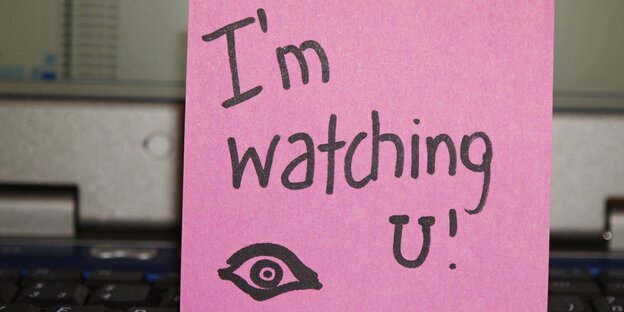 In einer Computertastatur steckt ein Zettel mit der Aufschrift: "I'm watching you". In einer Computertastatur steckt ein Zettel mit der Aufschrift: "I'm watching you".