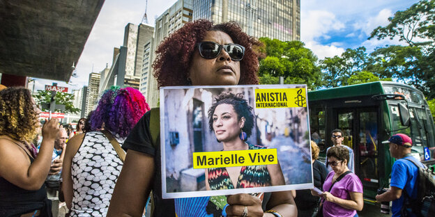 Schwarze Frau mit Sonnenbrille hält ein Schild in der Hand mit einem Foto von Marielle Franco und dem Slogan: "Marielle Vive" Schwarze Frau mit Sonnenbrille hält ein Schild in der Hand mit einem Foto von Marielle Franco und dem Slogan: "Marielle Vive"
