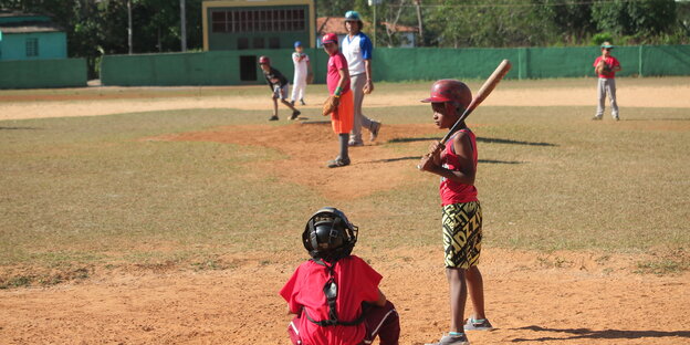Kinder spielen auf einem spärlich mit Gras bewachsenen Platz Baseball Kinder spielen auf einem spärlich mit Gras bewachsenen Platz Baseball