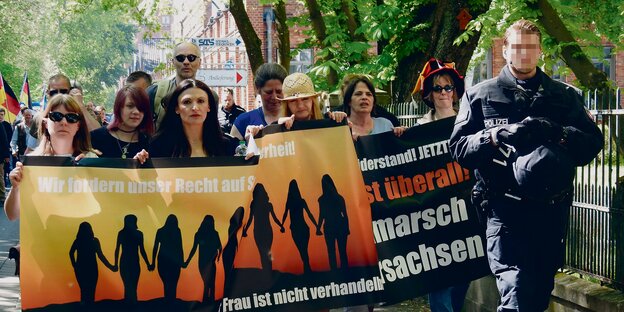 Frauen, die Demo-Plakate tragen und von einem Polizisten Geleitschutz bekommen. Frauen, die Demo-Plakate tragen und von einem Polizisten Geleitschutz bekommen.