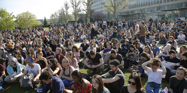 StudentInnen sitzen vor einer Universität auf dem Rasen StudentInnen sitzen vor einer Universität auf dem Rasen