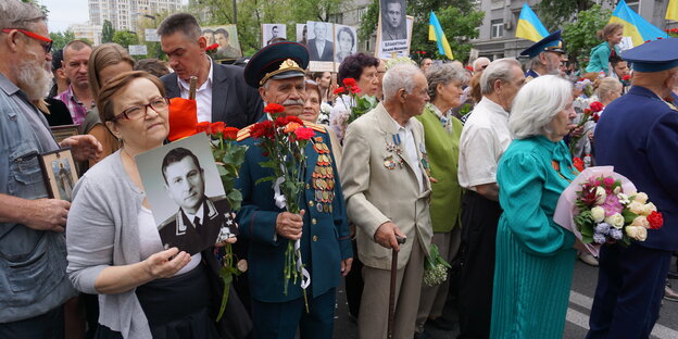 Menschen mit Blumen, Bildern Verstorbener und ein Mann in einer Uniform der Roten Armee Menschen mit Blumen, Bildern Verstorbener und ein Mann in einer Uniform der Roten Armee
