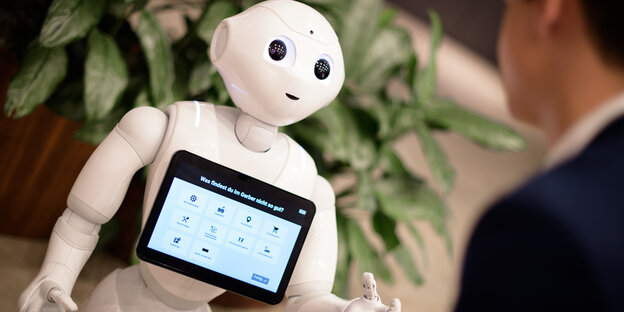 Ein Roboter mit Display auf der Brust begrüßt einen Besucher Ein Roboter mit Display auf der Brust begrüßt einen Besucher