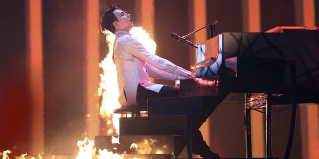 Ein Mann am Klavier, um ihn herum lodern Flammen Ein Mann am Klavier, um ihn herum lodern Flammen