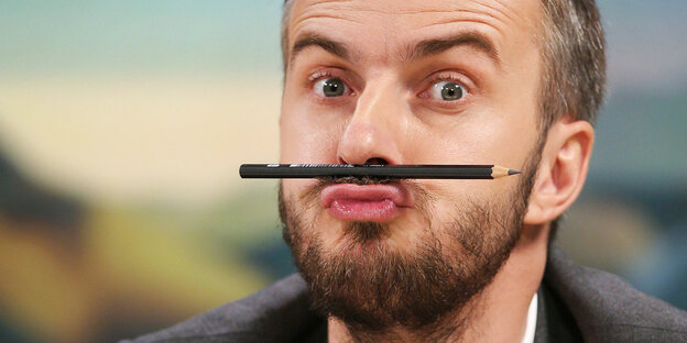 Jan Böhmermann hat einen Stift zwischen Oberlippe und Nase eingeklemmt und zieht dabei eine Grimasse Jan Böhmermann hat einen Stift zwischen Oberlippe und Nase eingeklemmt und zieht dabei eine Grimasse