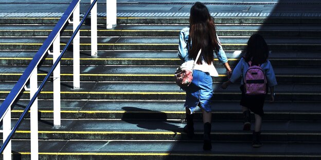 Eine Frau geht mit einem kleinen Kind Treppen hinauf