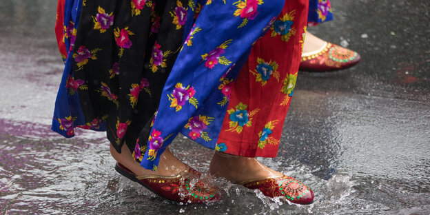 Teilnehmerinnen des Karneval der Kulturen in 2017 laufen in bunten Kostümen durch eine Regenpfütze Teilnehmerinnen des Karneval der Kulturen in 2017 laufen in bunten Kostümen durch eine Regenpfütze
