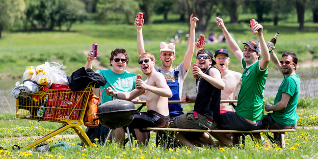 Auf Bänken sitzt eine Gruppe zum Teil unbekleideter Männer, in der Hand Bierdosen, daneben ein voller Einkaufswagen mit Bier Auf Bänken sitzt eine Gruppe zum Teil unbekleideter Männer, in der Hand Bierdosen, daneben ein voller Einkaufswagen mit Bier